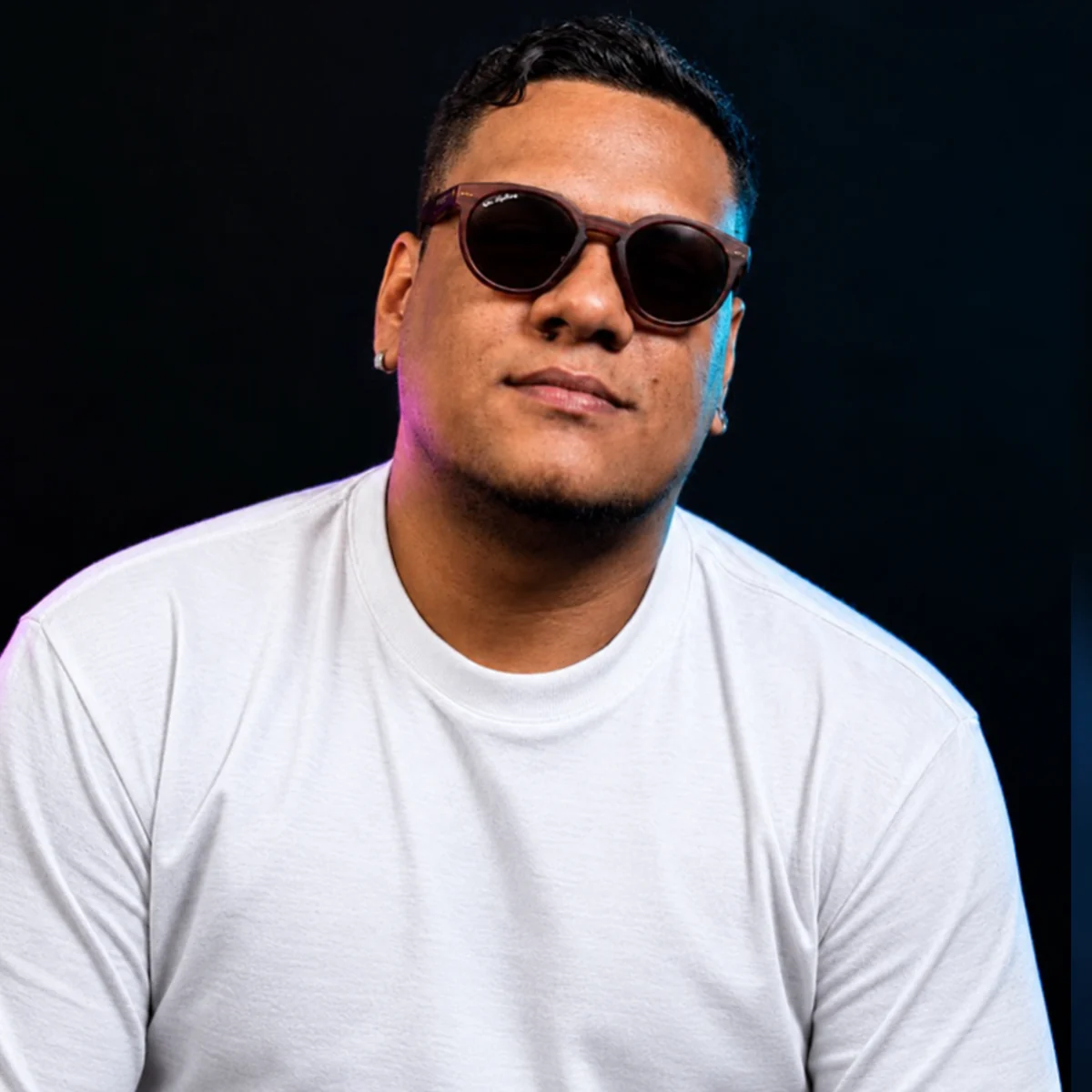 Retrato de Erick Fernandes, co-founder da identidade, de óculos escuros e camiseta branca sobre fundo escuro
