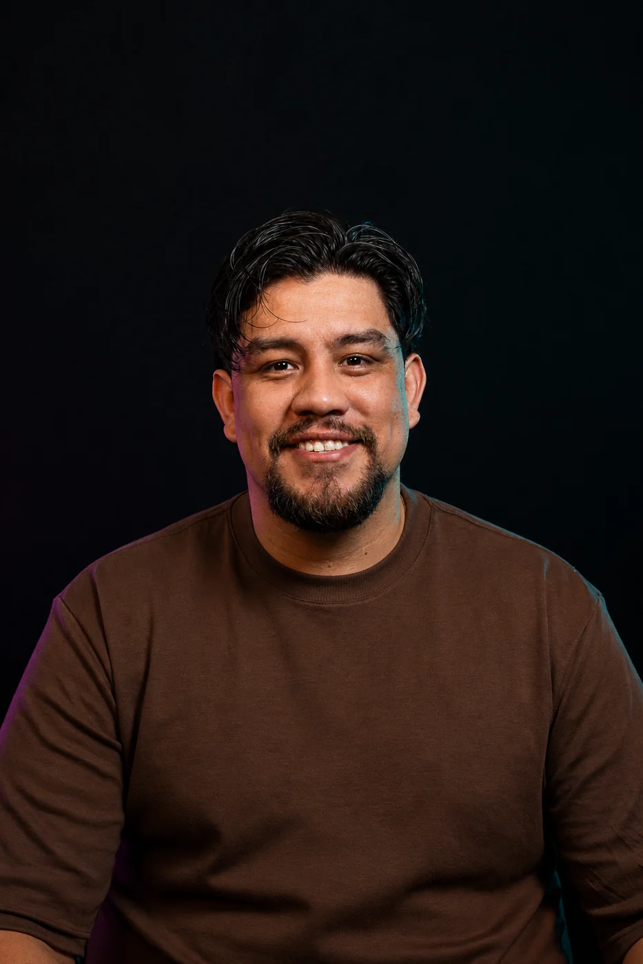 Retrato de Patrick Lins, co-founder da identidade, sorrindo, de camiseta marrom sobre fundo escuro